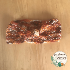A toddler headband in the shape of a bow at the front. In a brown, burnt orange, cream and brown varigated yarn.