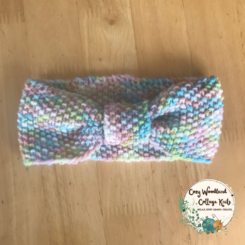 A toddler headband in the shape of a bow at the front. In a pink, light blue. white, lime and blue varigated yarn.
