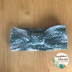 A toddler headband in the shape of a bow at the front. In a white and green varigated yarn.