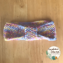 A toddler headband in the shape of a bow at the front. In a yellow, white, pink, purple varigated yarn.