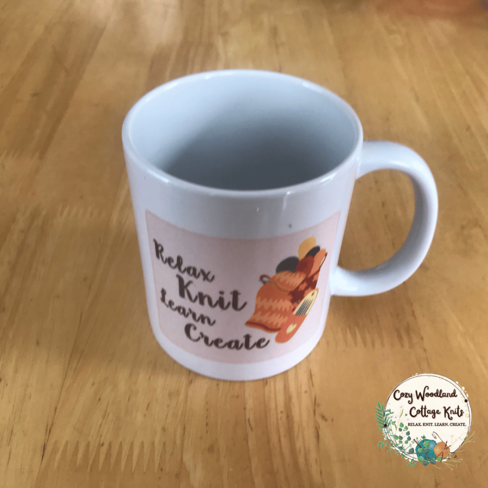 A knitting mug with a pink rectangle with the words "relax knit learn create". Next to it is a basket of yarn, a knitted blanket and a needle case.